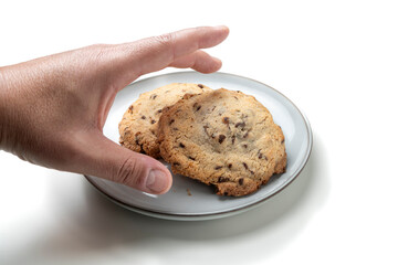 Hand reaching for chocolate chip cookies on white plate