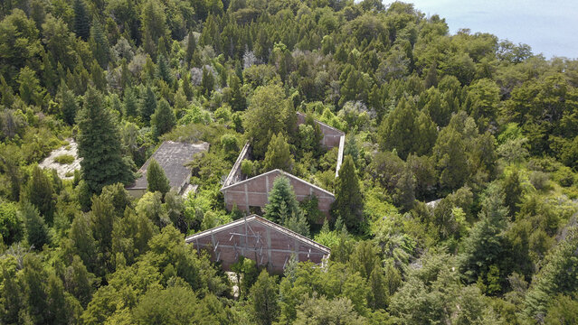 Aerial view of abandoned buildings swallowed by a dense forest canopy, a haunting contrast of decay and vibrant nature, San Carlos de Bariloche, Rio Negro Province, Argentina.