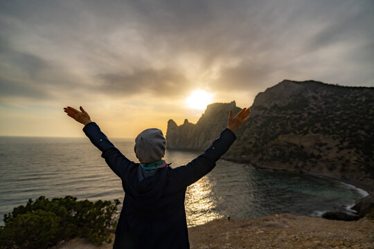 Woman sunset freedom standing on a cliff edge overlooking the ocean with raised arms - Powered by Adobe
