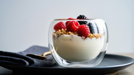 Modern double-wall glass cup filled with yogurt, crunchy granola and fresh berries on dark plate, showcasing elegant borosilicate design for minimalist, heat-resistant and aesthetic food presentation