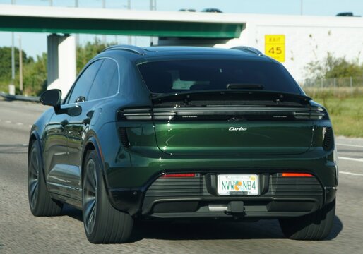 Lakeland, Florida, U.S - Nov 10, 2025 - A rear view of a dark green Porsche Taycan Cross Turismo Turbo driving on a highway, passing under an overpass