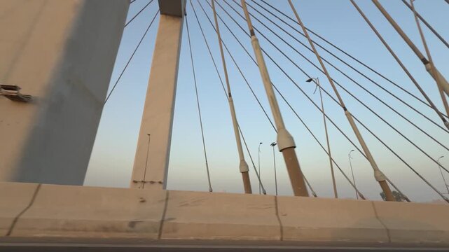 Low angle driving shot capturing the massive cables and pylons of the Tahya Misr Bridge (Rod El Farag Axis) against a blue sky