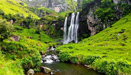 Waterfall cascades down mossy cliffs into a serene stream flowing through a lush green valley