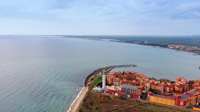 Colorful residential Marina Cape complex in Aheloy, Bulgaria with a lighthouse. Scenery of the Black Sea waterscape merging with the overcast sky. Aerial view.