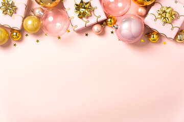 Pink and gold Christmas ornaments, bows, and small gifts arranged on a soft pastel pink background.