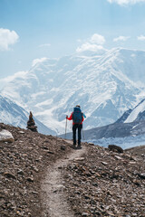 Fototapeta premium Lonely Climber woman with backpack and trekking poles during Lenin peak ascent with mountain peaks and glaciers in background. Extreme active people, high-altitude mountaineering concept image