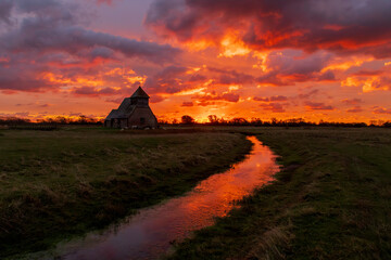The iconic St Thomas à Becket Church on Fairfield, Kent stands silhouetted against a blazing...