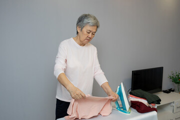 An elderly Asian woman ironing clothes at home