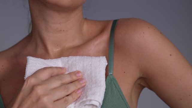 Young woman wiping sweat from her chest and neck with a towel after an intense workout. Post-training cooling down routine and natural skin texture