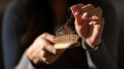 Woman holding strands of fallen hair on wooden brush visual sign of hair shedding, stress-induced hair loss, hormonal imbalance, or seasonal telogen effluvium personal care and health concern 