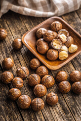 Tasty macadamia nuts in bowl on wooden table.