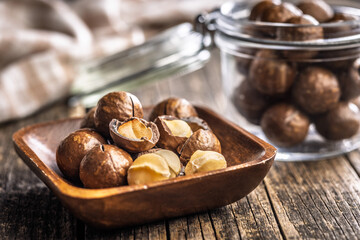 Tasty macadamia nuts in bowl on wooden table.