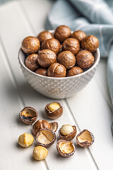 Tasty macadamia nuts in bowl on white table.