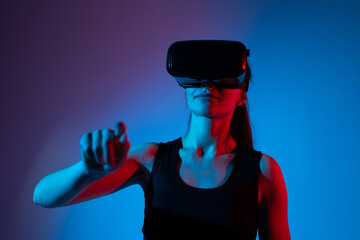 Gamer woman reaching toward virtual elements while using VR headset under neon lighting effects