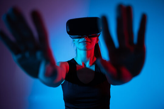 Woman interacting with virtual reality interface in neon blue and red light, exploring immersive VR space - Powered by Adobe