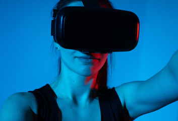 Woman interacting with virtual reality headset illuminated by dramatic blue and red futuristic light