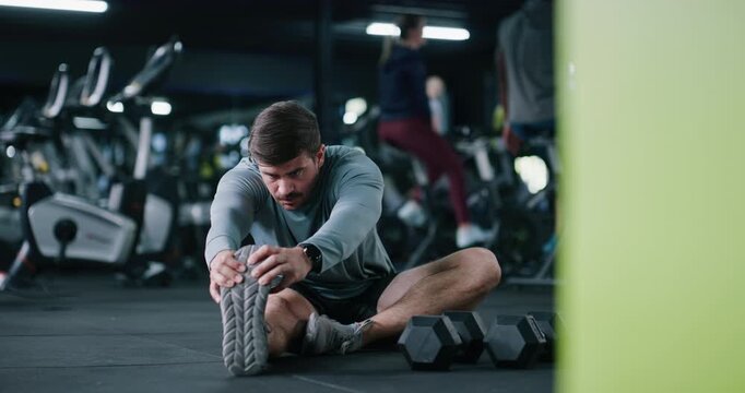 Exercise, legs and man stretching in gym for fitness, training or wellness routine in morning. Health, athlete and male person with warm up workout for preparing muscles on floor in sports center.