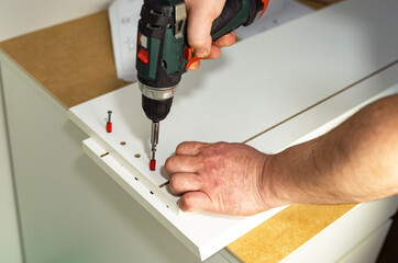 The process of assembling white cabinet furniture using a screwdriver