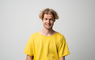 Smiling young man looking sideways with awkward amused expression while posing in neutral studio scene