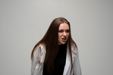 Fototapeta premium Young woman leaning forward with angry aggressive facial expression in minimalist studio portrait