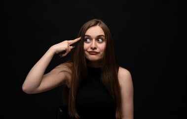 Portrait of a young woman making a thinking gesture with playful expression on a dark studio background