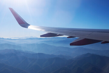 Fototapeta premium An aerial shot capturing layered mountain ridges illuminated by early sunlight, viewed from an airplane window. The aircraft wing frames the scene, adding a sense of travel, altitude