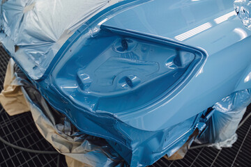 Professional car painting in a specialized spray booth at an auto service center. Body repair and surface preparation process. Quality maintenance and technical service for modern vehicle transport.