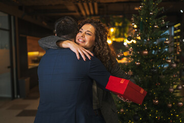 Office couple exchanging christmas gift and hugging during holiday party