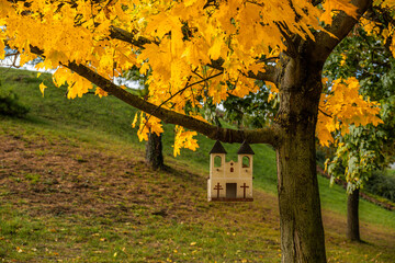 Autumn tree with decorative wooden church hanging on branch
