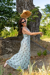 Woman playing with straw hat and dancing barefoot with a big smile in nature