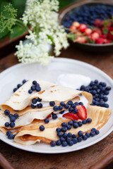 Delicious homemade crepes with fresh fruit  -  blueberry and alpine strawberry. Gourmet picnic snack ina spring garden.