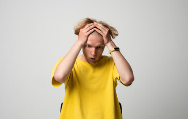 Surprised young man holding his head with both hands and reacting with shocked expression in studio