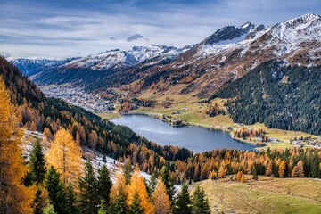 Alpine Valley Golden Larches Snow Dusted Peaks Under Expansive Blue Sky, Winding Hiking Trail Through Colorful Meadow And Rocky Ridge, Crisp Autumn. Autumn panorama in Davos with a view of the lake.