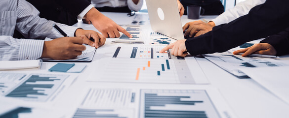 A diverse business team actively collaborating over charts and data in a modern office setting. Individuals engage with laptops, notepads, and digital tools for effective analysis. SACTR
