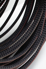 Black toothed drive belts arranged in a curved, repeating pattern on a white background. Abstract mechanical concept for automotive transmission, precision timing, and industrial power transfer soluti