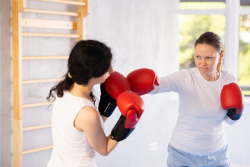 Focused woman practicing boxing punches in sparring during group self defence course in gym