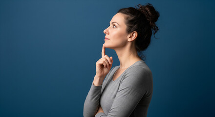 Fototapeta premium Thoughtful Woman Pondering a Complex Problem in Profile A profile medium shot of a focused woman, deep in thought, with her finger resting thoughtfully on her chin. Her hair is neatly tied up in a bun