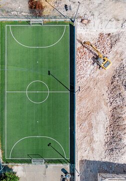 Aerial view of a vibrant green sports field contrasted against the stark, rocky terrain where a yellow digger sits, Locorotondo, Apulia, Italy.
