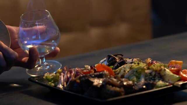 A person holding a glass of wine over a plate of food