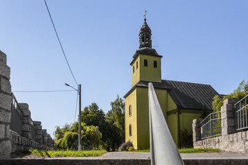 Obraz premium Side Perspective of the Roman Catholic Green Church Under Blue Sky in Modliszewko, Gniezno Commune, Poland with Stone Wall and Handrail