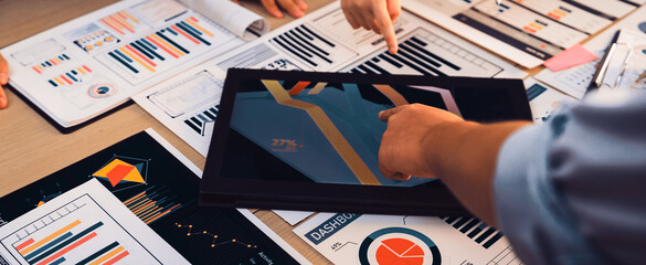 A diverse team collaborates in a modern office, engaging in data analysis. They use a digital tablet displaying colorful infographics while discussing charts and reports. SACTR