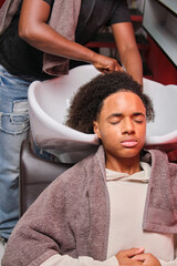 Afro man having his hair rinsed at salon sink with eyes closed by hairstylist