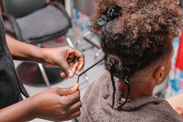 Afro young man getting African braids styled by hairstylist from rear view