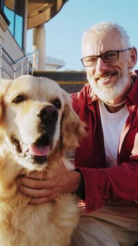 Old man with glasses pets golden retriever on stone steps