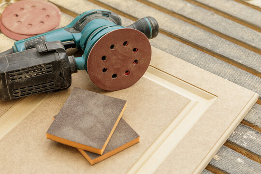 Orbital sander and sanding pads on cabinet door panel in carpentry workshop
