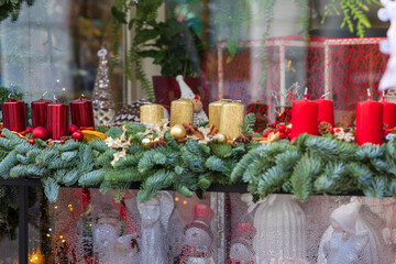 Festive Christmas window display with garland, red, and gold candles. A close-up shot of a festive Christmas shop window display, the lower section of which is decorated with a lush, dark green