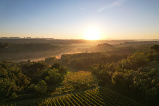 Aerial view of golden sunlight spills over the rolling hills and vineyards of Tuscany at dawn, casting long shadows and painting the landscape in warm hues, Le Tolfe, Tuscany, Italy.