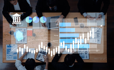 Business professionals collaborate in a modern office setting, analyzing financial data on laptops and charts while utilizing digital tools for strategic planning. Gantry