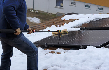 Ein Mann befreit eine Photovoltaik Anlage auf einem Dach vom Schnee