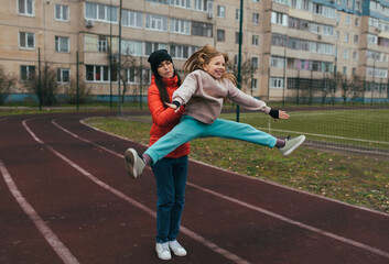 A beautiful, happy teenage girl, a gymnast, a cheerleader, and a female coach (her mother) train together, performing complex exercises, on a treadmill outside at a stadium. Photo, sports concept.